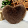 A fluffy, heart-shaped brown faux fur throw pillow resting on a light-colored sofa.