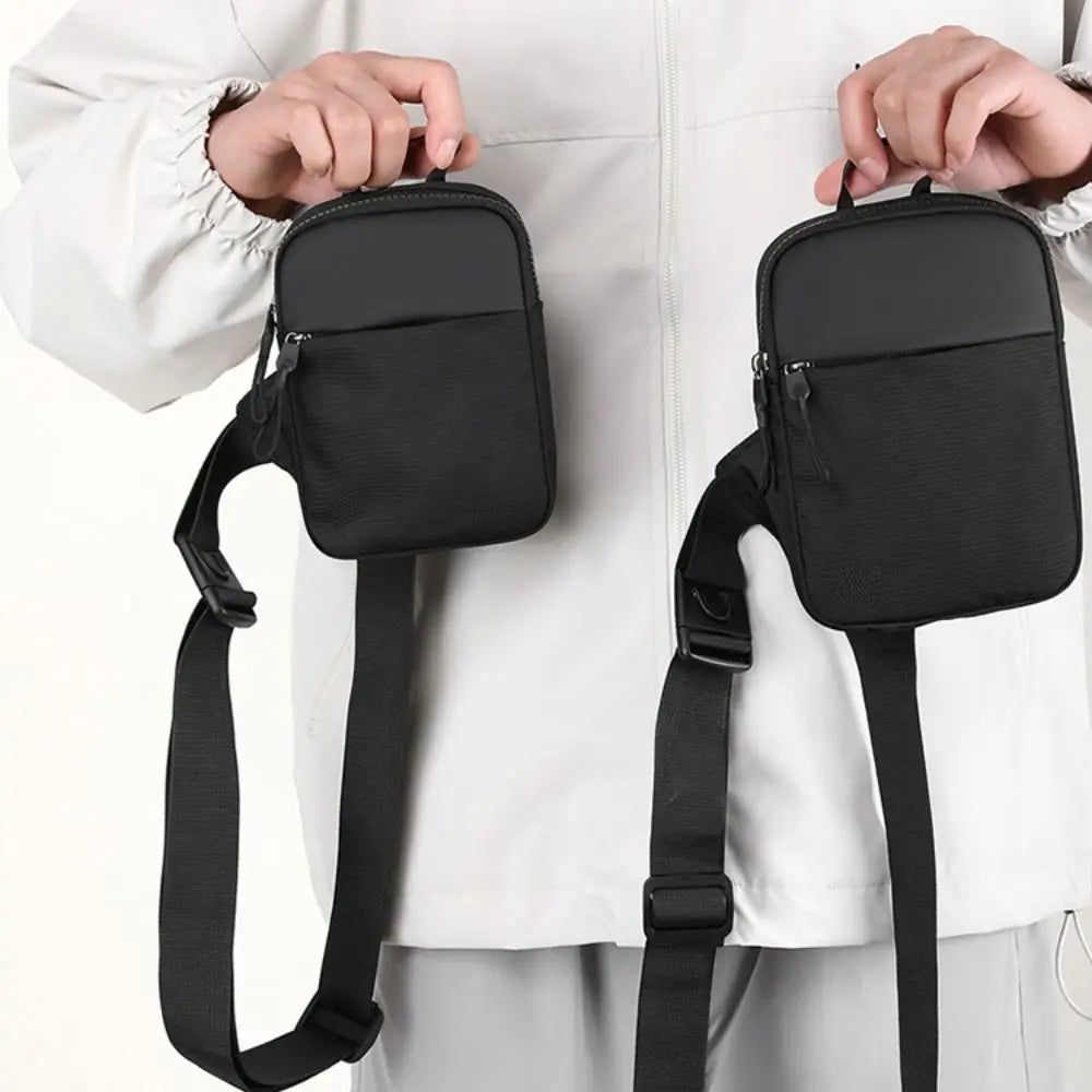 A black canvas crossbody sling bag being held by a person against a white shirt.