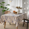 A beige cotton-linen tablecloth with a blue rustic fern print set on a wooden table.