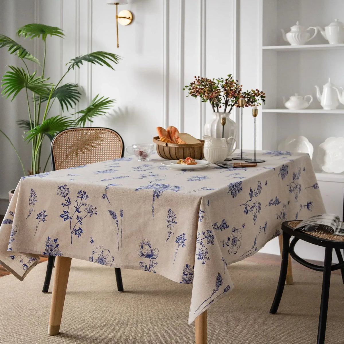 A beige cotton-linen tablecloth with a blue rustic fern print set on a wooden table.
