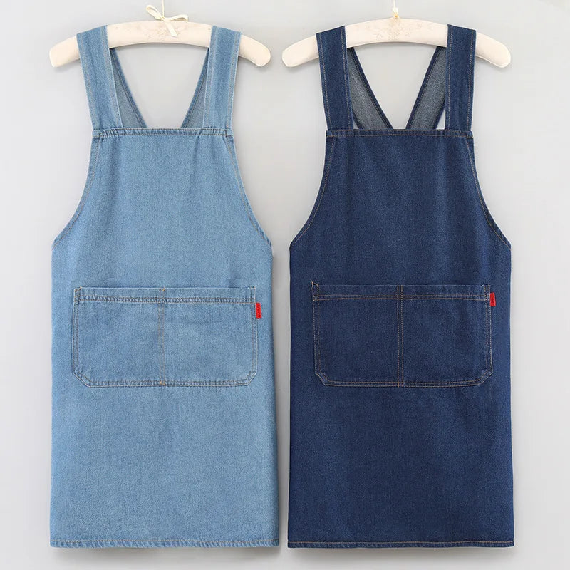 A pair of heavy-duty washed denim cross-back aprons in blue and navy are displayed on hangers.