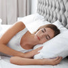 A woman is sleeping comfortably on a bed with white pillows, holding a white pillow close.