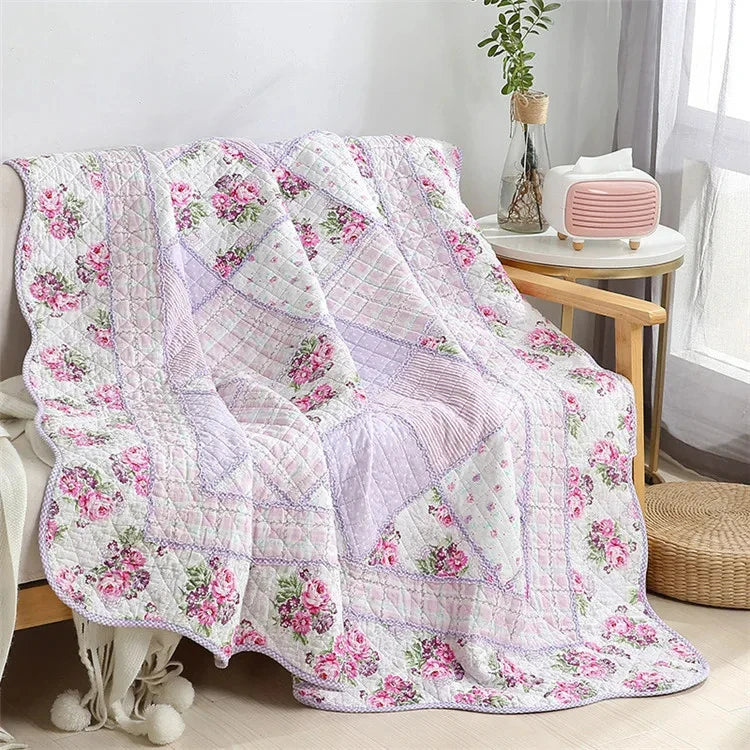 A pink and white floral patchwork quilt with embroidery draped on a light-colored surface.