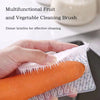 Une main tient une brosse en silicone orange pour nettoyer les fruits et légumes.
