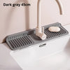 Dark gray silicone faucet splash mat with a faucet and soap dish mounted on a white countertop.