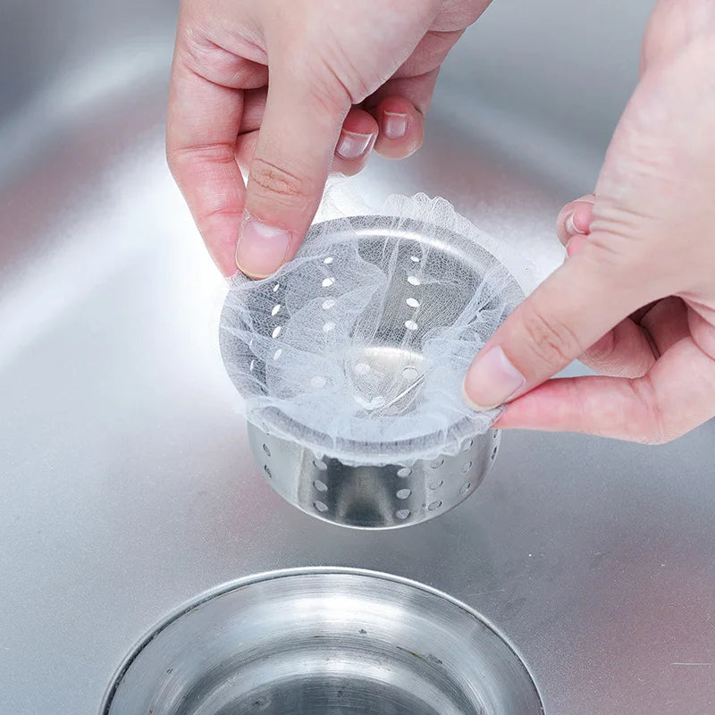 A hand is placing a disposable sink drain filter into a metal strainer, demonstrating the product.