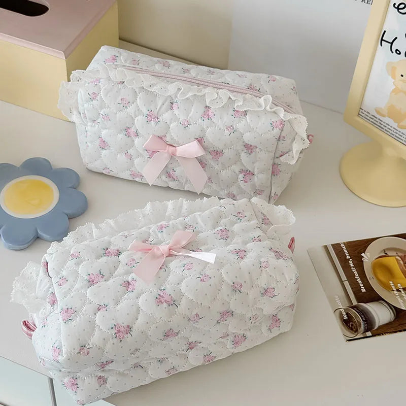 White cosmetic pouch with a vintage rose print and pink lace trim resting on a white surface.