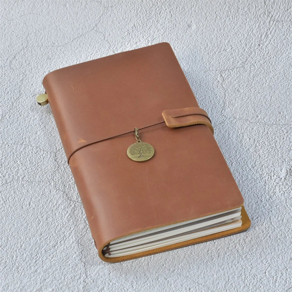 A brown leather refillable journal with a brass clasp resting on a light gray textured surface.