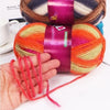 A hand is holding a skein of gradient dyed wool blend yarn featuring shades of orange, pink, and yellow.