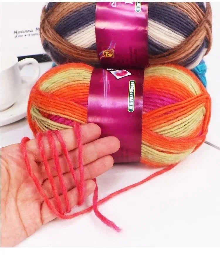 A hand is holding a skein of gradient dyed wool blend yarn featuring shades of orange, pink, and yellow.