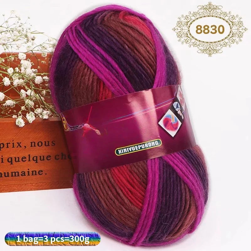 A skein of gradient dyed wool blend yarn in shades of purple, pink, and red is shown next to a box.