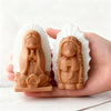 A hand holds two silicone molds shaped like praying girls, used for candles, soap, and craft decor.