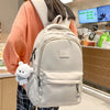 A light beige waterproof nylon laptop backpack is worn by a person in a brightly lit indoor setting.