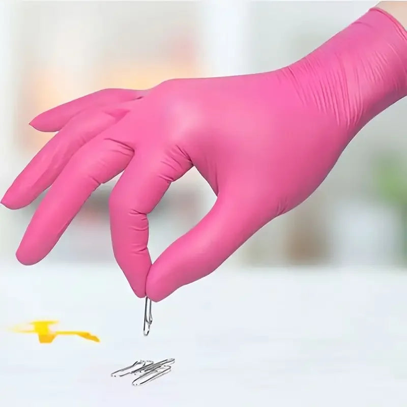 A hand wearing a bright pink nitrile disposable glove is shown holding a small metal object on a white surface.