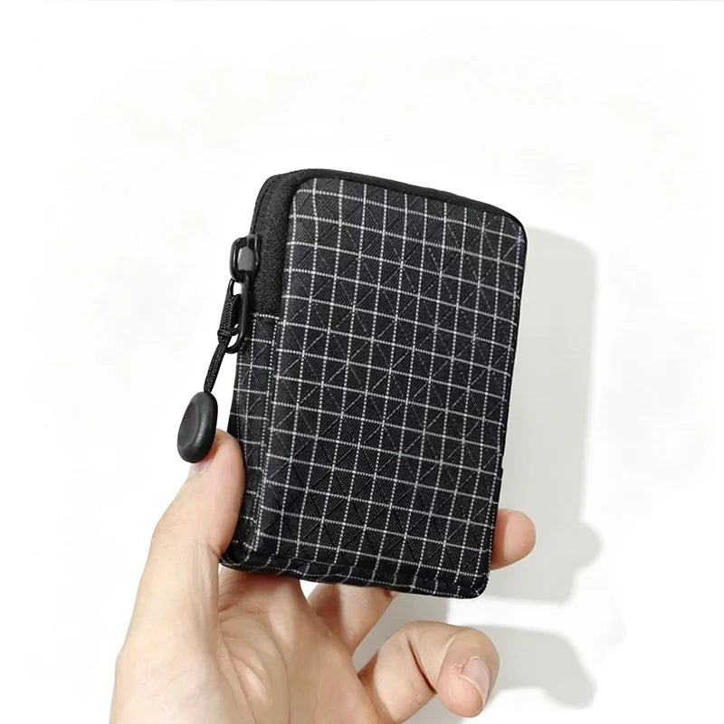 A hand holds a black compact EDC utility pouch featuring a fine grid pattern.