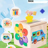 A wooden color classification box with various colored shapes and a yellow sorting tool, set in a grassy outdoor context.