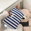 Pochette en crochet à rayures bleu marine et blanc posée sur une surface blanche à côté d'un grand jouet en peluche.