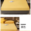 Protector impermeable amarillo para colchón, mostrado en una cama con almohadas y mesita de noche.