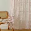 Pink ruffled French lace sheer curtains with floral embroidery covering a window.