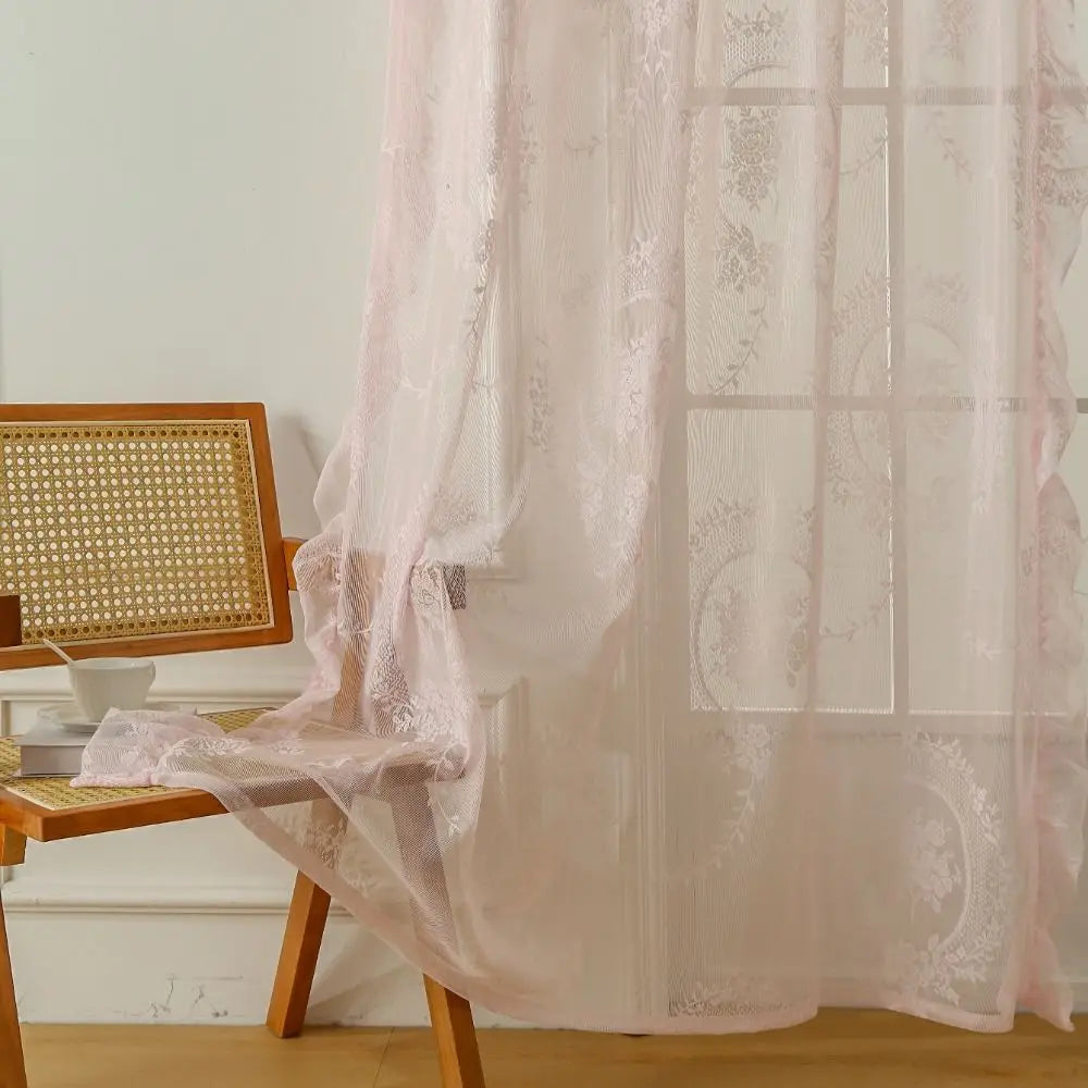 Pink ruffled French lace sheer curtains with floral embroidery covering a window.