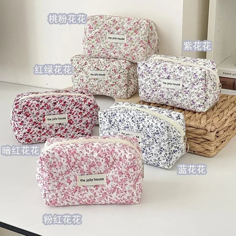A collection of quilted floral makeup bags in various pink and white patterns are displayed on a white surface.