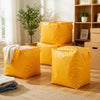 A stack of bright yellow waterproof moving and storage bags on a wooden floor next to a window.