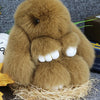 A fluffy brown bunny keychain with a pom pom tail resting on straw.