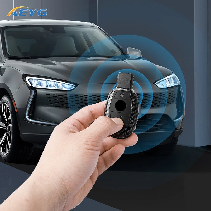 A hand holds a slim carbon fiber car key cover near the headlight of a dark gray car.