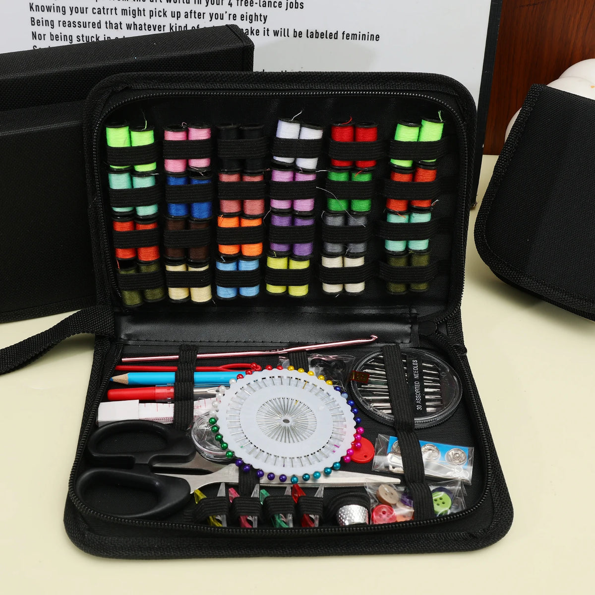 A black portable multi-function sewing kit is shown open, displaying various threads, needles, and tools in compartments.