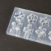 A clear silicone mold containing various floral shapes for nail art and beauty applications.
