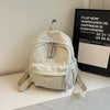 A light beige Japanese corduroy casual backpack is displayed on a white surface next to a framed sign.