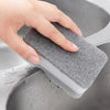 A hand is holding a gray, reusable double-sided cleaning sponge inside a gray sink.