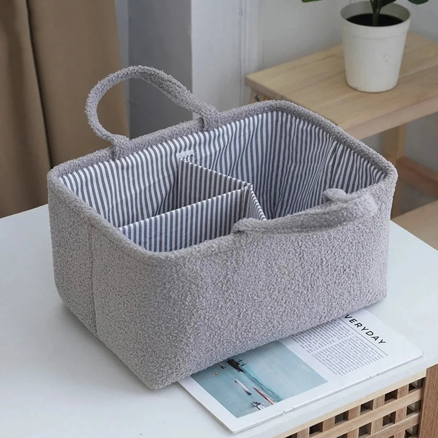 A gray fabric portable diaper bag organizer with striped interior and a handle is shown on a white surface.