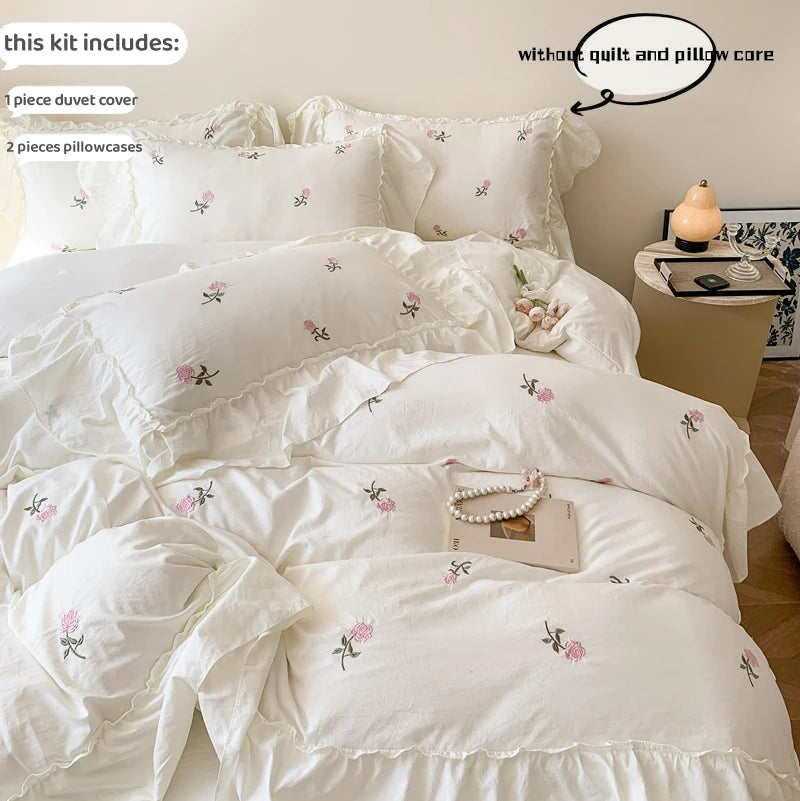White duvet cover set with pink rose embroidery and lace details displayed on a bed.