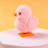 A pink fluffy wind-up walking chicken toy with orange feet standing on a white surface.
