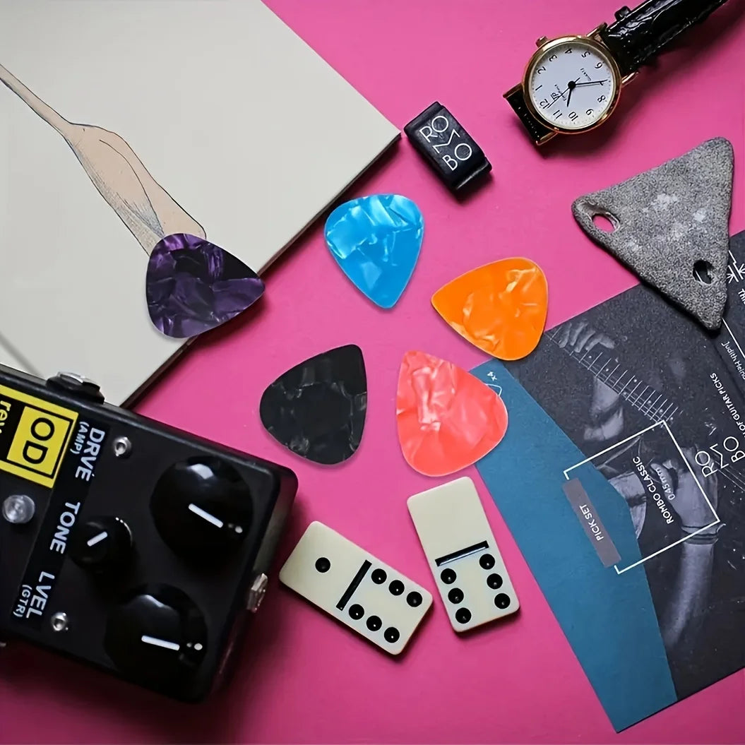 A collection of assorted guitar picks in various colors and thicknesses scattered on a pink surface.