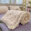 A rolled floral washed cotton gauze fabric in pale lavender and cream tones resting on a purple surface.