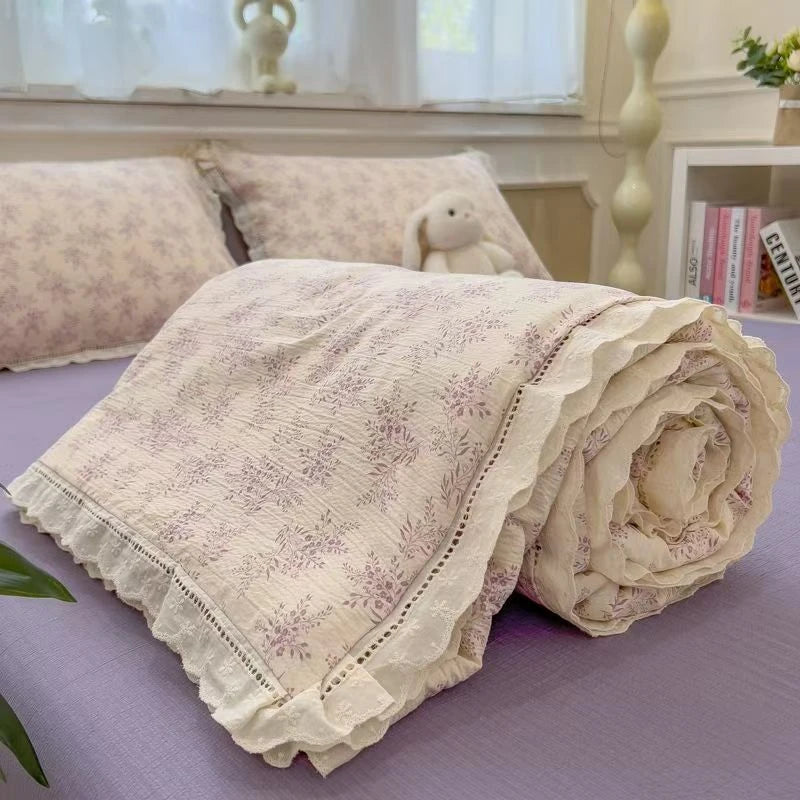 A rolled floral washed cotton gauze fabric in pale lavender and cream tones resting on a purple surface.