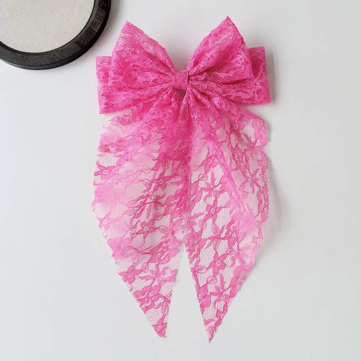 A bright pink lace bow accessory for a hair clip or ponytail, featuring intricate floral patterns.