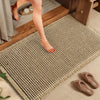 A beige waffle weave bath mat with tassels is placed on a wooden floor next to a door.