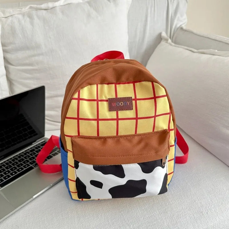 A brown and yellow plaid backpack with a cow print patch and red straps resting on a white surface.