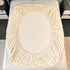 A round, thick knit fitted bed sheet in cream color with a textured, ribbed edge.