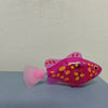 A pink light-up sensor swimming fish toy with yellow spots resting on a gray surface.