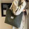 A light beige corduroy tote bag is carried by a person, with a black sign visible in the background.