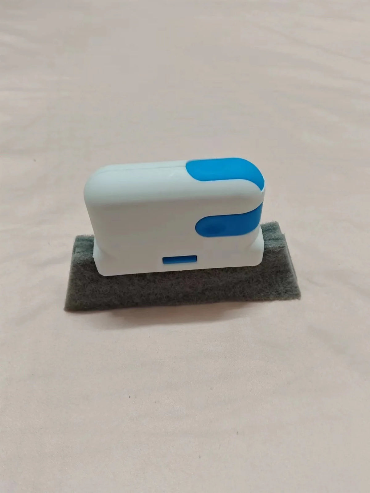A white and blue multi-purpose crevice cleaning brush resting on a gray felt surface.