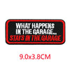 Black embroidered iron-on letter patch with red text that reads What Happens In The Garage Stays In The Garage