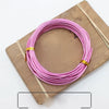 Pink and silver anodized aluminum jewelry wire coiled on a wooden board