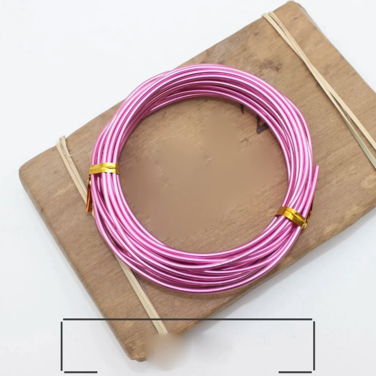 Pink and silver anodized aluminum jewelry wire coiled on a wooden board