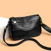 A black leather compact square crossbody bag with a silver charm and black strap.