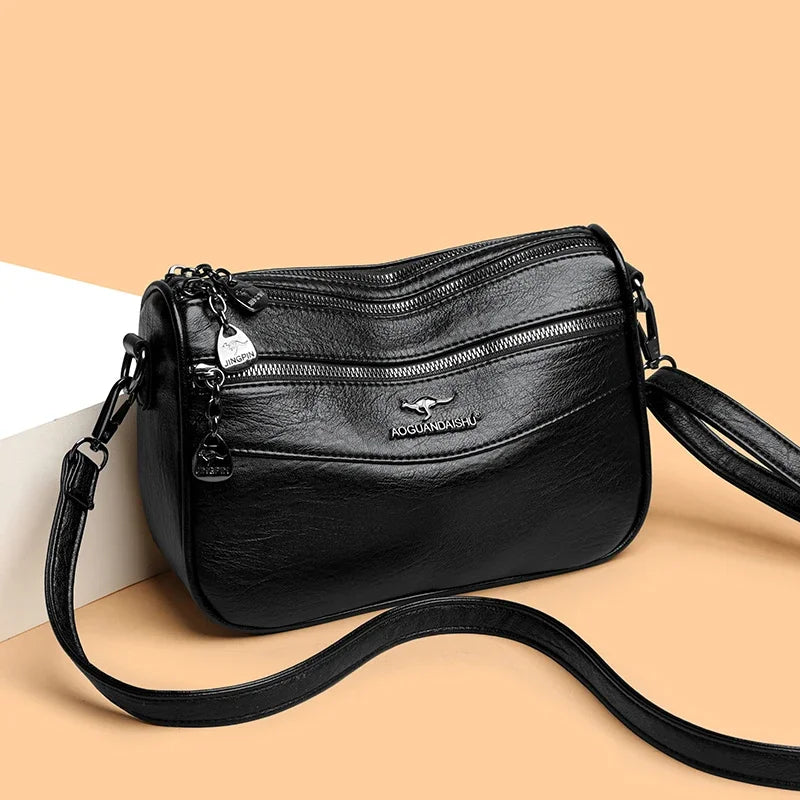A black leather compact square crossbody bag with a silver charm and black strap.
